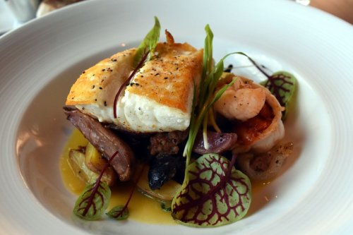 A beautifully plated dish featuring seared fish, shrimp, and colorful garnishes on a bed of vegetables.