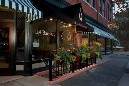Exterior of a restaurant with a sign reading "114 Barnard," featuring flower planters and striped awnings.