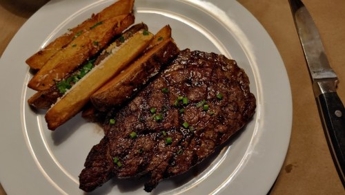A plate featuring a juicy steak garnished with herbs, accompanied by crispy potato wedges.