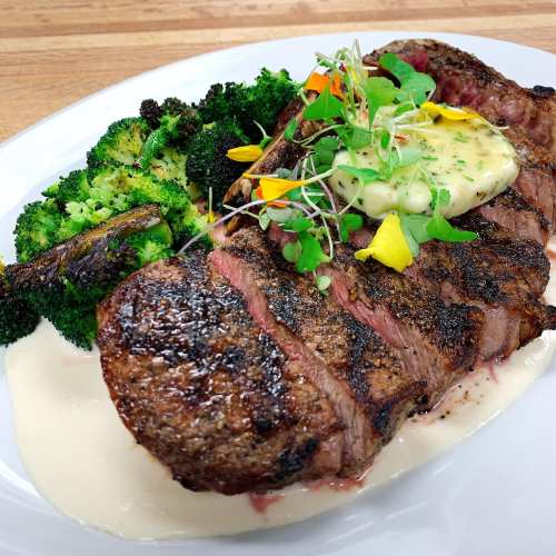 A beautifully plated steak with herb butter, served with roasted broccoli and a creamy sauce on a white plate.