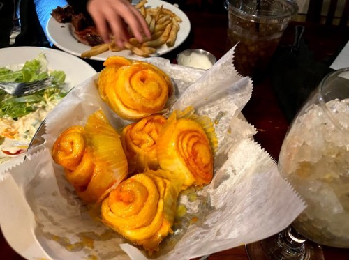 A basket of golden, spiral-shaped pastries sits on a table, with fries and drinks in the background.