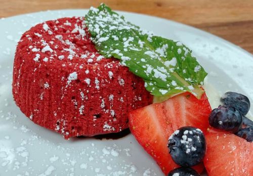 A red velvet dessert topped with powdered sugar, garnished with mint and served with strawberries and blueberries.