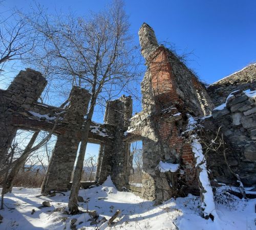 Ruins of a stone structure surrounded by snow and trees under a clear blue sky.