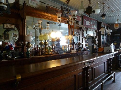 A vintage bar with a wooden counter, antique lamps, and mirrors, showcasing a nostalgic atmosphere.