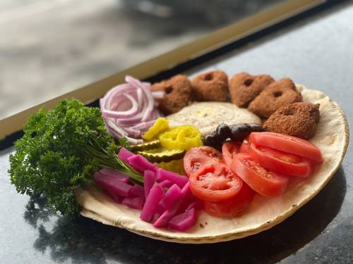 A colorful plate featuring falafel, fresh vegetables, pickles, and herbs arranged on a flatbread.