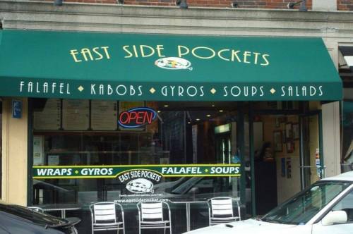 A storefront with a green awning reading "East Side Pockets," featuring menus for falafel, kabobs, and gyros.