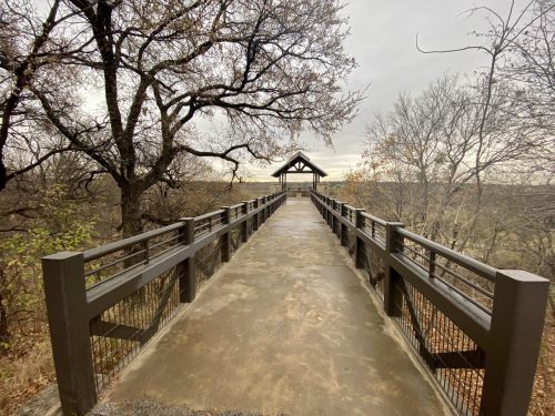 A wide, empty pathway leads to a gazebo, surrounded by trees and a cloudy sky.