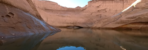 A serene canyon landscape with smooth rock formations reflected in calm water.