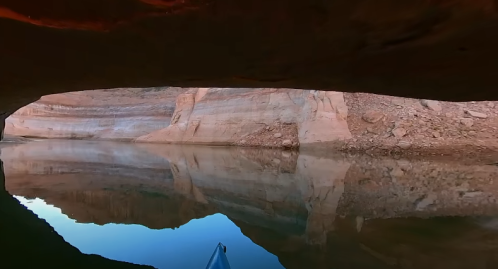 A serene view from under a rock overhang, reflecting calm water and canyon walls in warm tones.