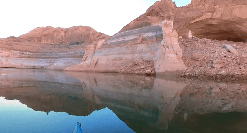 A serene lake scene with rocky cliffs reflecting in calm water at sunrise.