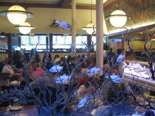 A bustling restaurant interior with diners, featuring decorative fish and coral designs on the glass.