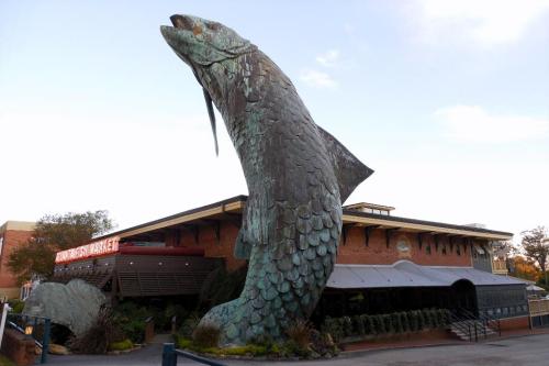 A large bronze fish sculpture stands outside a market, showcasing its detailed scales and dynamic pose.