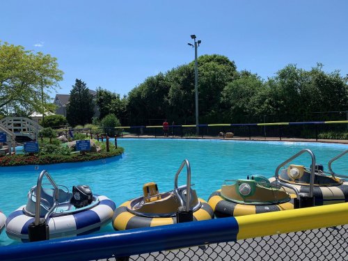 A sunny day at a water park featuring colorful bumper boats in a blue pool surrounded by greenery.