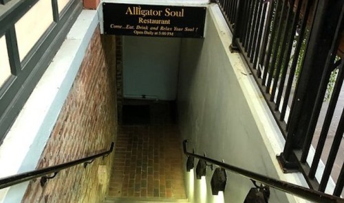 Stairs leading down to Alligator Soul Restaurant, with a sign inviting guests to eat and relax.