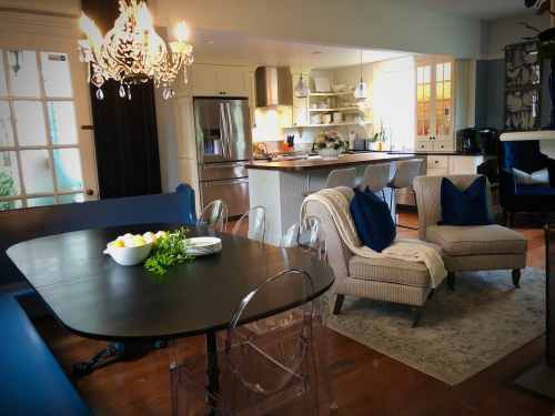 A cozy kitchen and dining area featuring a table, chairs, and a stylish chandelier, with light streaming in.
