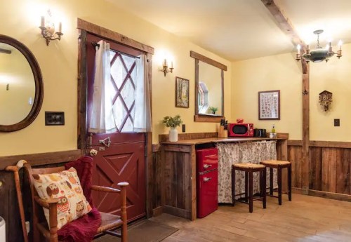 Cozy interior with yellow walls, wooden accents, a red fridge, and a welcoming door, featuring rustic decor and seating.