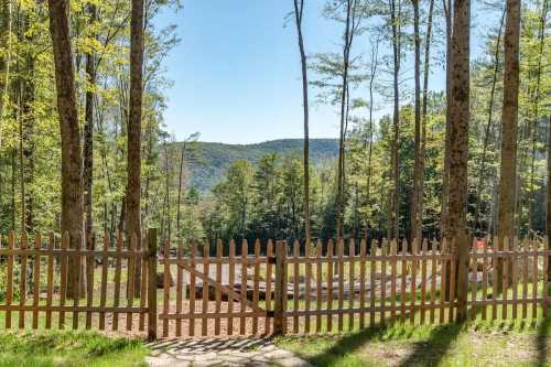 A wooden fence opens to a scenic view of green trees and distant mountains under a clear blue sky.