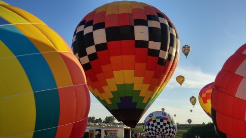 Colorful hot air balloons in various patterns ascend against a clear blue sky during a festival.