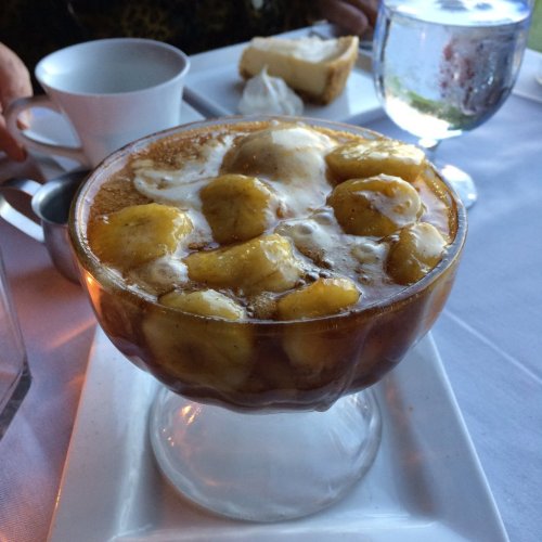 A glass dish filled with sliced bananas, ice cream, and a caramel sauce, served on a white tablecloth.