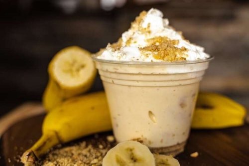 A creamy banana dessert topped with whipped cream and crushed graham crackers, served in a clear cup with bananas nearby.