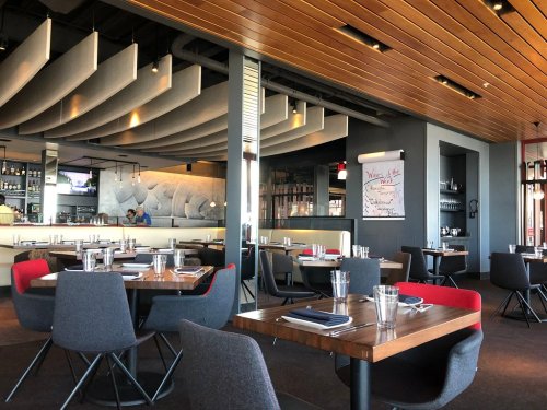 Modern restaurant interior with wooden accents, stylish seating, and a bar area in the background.
