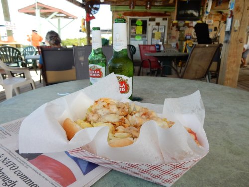 A table with a basket of food, two beers, and a newspaper in a casual outdoor dining setting.