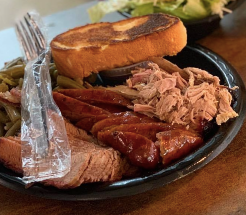 A plate of barbecue featuring sliced meats, green beans, toast, and a side salad.