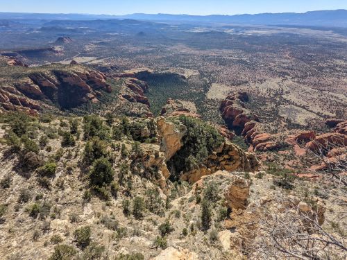 A panoramic view of rugged red rock formations and expansive desert landscape under a clear blue sky.
