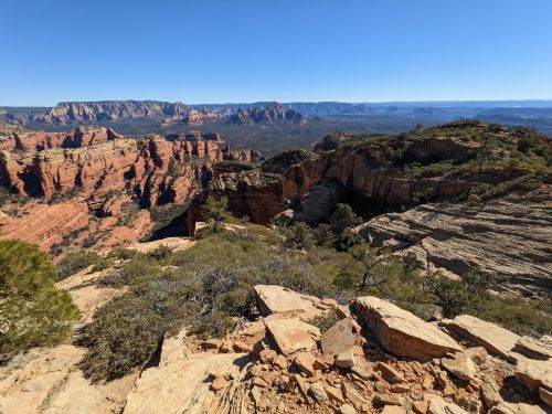 A panoramic view of rugged red rock formations and distant mountains under a clear blue sky.