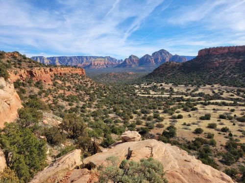 A scenic view of red rock formations and green valleys under a blue sky with wispy clouds.