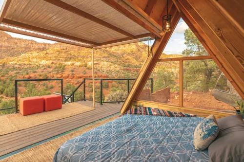 Cozy A-frame bedroom with a view of red rock mountains and outdoor seating area. Warm, inviting interior.