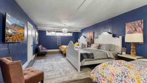 A spacious bedroom with blue walls, two beds, a TV, and decorative artwork, featuring a cozy seating area.