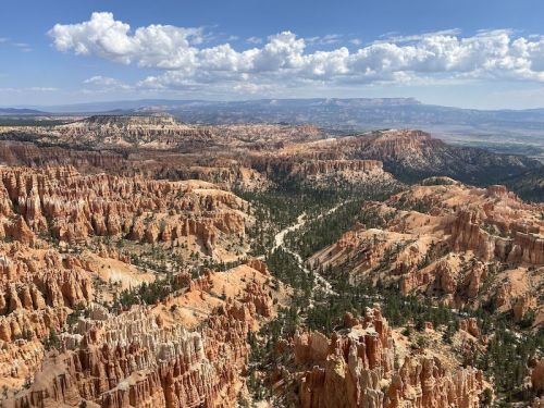 A panoramic view of Bryce Canyon's colorful rock formations and lush greenery under a blue sky with fluffy clouds.