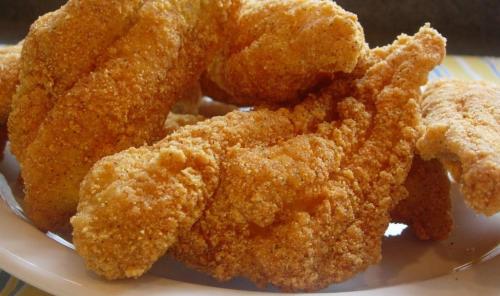 A close-up of golden-brown, crispy fried fish fillets arranged on a white plate.