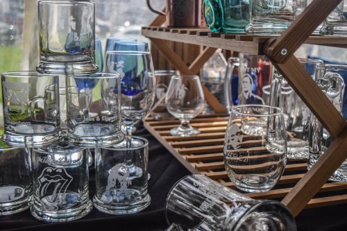 A display of various glassware, including engraved mugs and tumblers, arranged on a wooden rack.