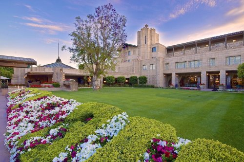 A landscaped garden with colorful flowers in front of a large, elegant building under a clear blue sky.