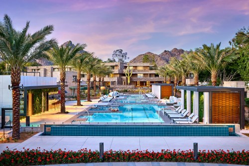 A luxurious pool area surrounded by palm trees and mountains, featuring lounge chairs and vibrant flowers.