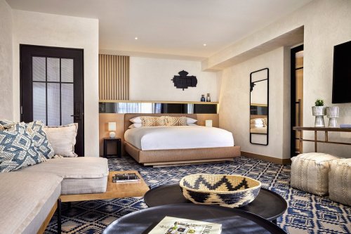 A modern hotel room featuring a large bed, cozy seating area, and stylish decor with neutral tones and patterned accents.