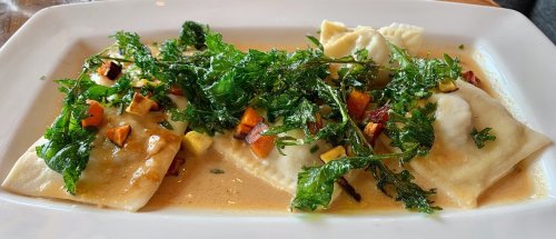 A plate of ravioli topped with sautéed greens and diced vegetables in a light sauce.