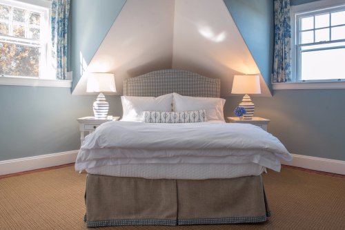 Cozy bedroom with a sloped ceiling, a bed with white linens, two lamps, and light blue walls.