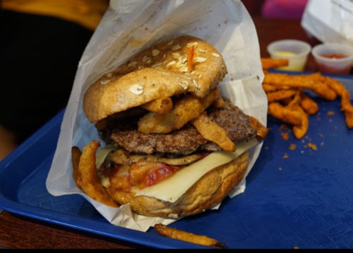 A hearty burger with two patties, cheese, crispy onion rings, and a whole grain bun, served with sweet potato fries.