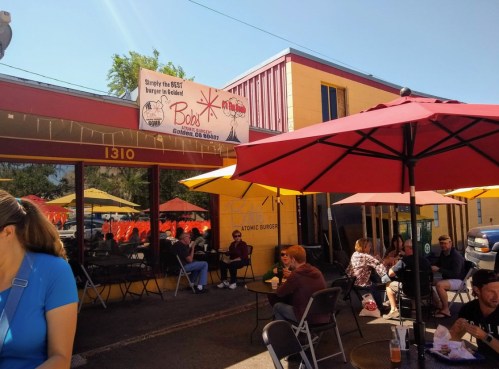 A colorful restaurant exterior with outdoor seating and umbrellas, featuring a sign for Bob's Atomic Burgers.