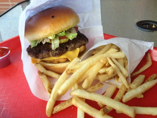 A cheeseburger with lettuce, tomato, and a side of golden French fries on a red tray.