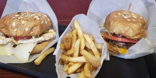 Two burgers on whole grain buns with toppings, alongside a serving of golden French fries.
