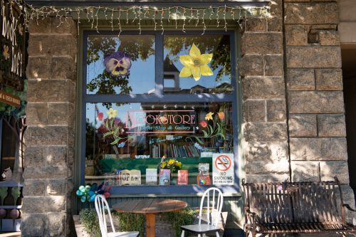 A charming bookstore window adorned with flowers and books, featuring a "No Smoking" sign and outdoor seating.