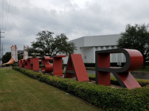 Large red and white letters spelling "WILDSTAR" in front of a building, surrounded by green grass and trees.