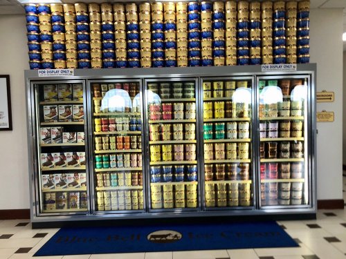 A large display freezer filled with various ice cream tubs, surrounded by stacked containers on the wall.