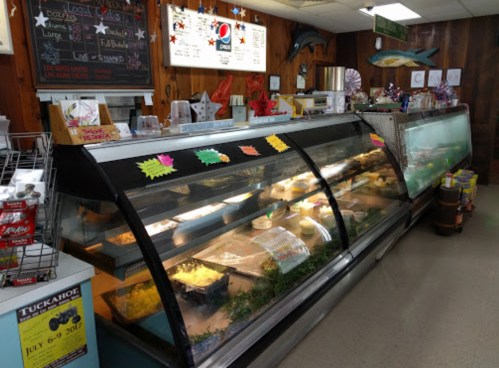 Display case filled with various food items in a cozy, rustic eatery with a chalkboard menu and colorful decorations.