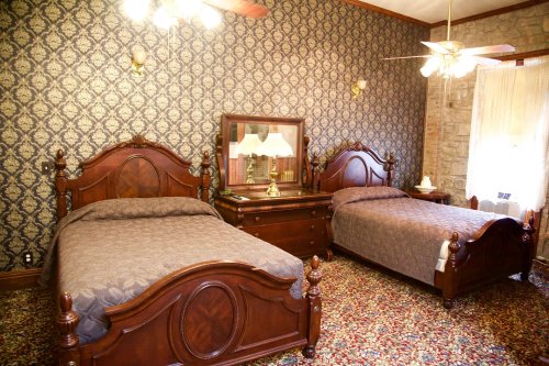 A vintage bedroom featuring two wooden beds, a dresser with a mirror, and patterned wallpaper.