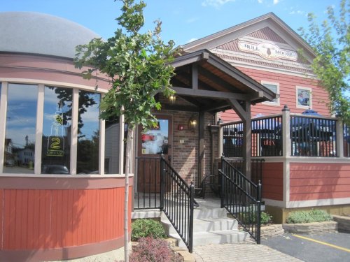Exterior view of a restaurant featuring a brick facade, a covered entrance, and outdoor seating.